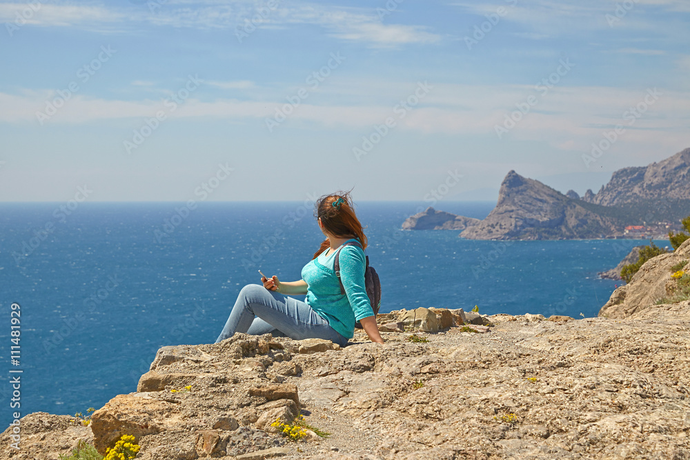 Woman looks at the edge of the cliff on the  sea bay of mountains in the background