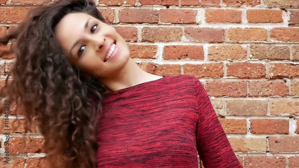 Portrait of happy young woman shaking her beautiful curly hair on brick wall, slow motion Portrait of happy young woman shaking her beautiful curly hair on brick wall, slow motion