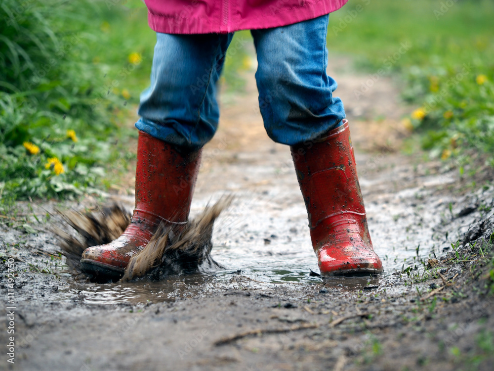 child's feet in the muddy, wet jeans and rubber boots. The child jumps in a  puddle Stock Photo | Adobe Stock