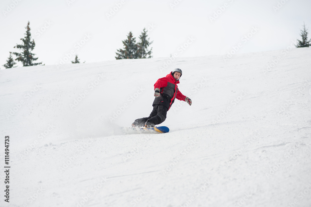 Young male snowboarder riding over the slope at the mountains overlooking a ski run on the snowy slope below at a winter resort, extreme sport. Bukovel, Ukraine