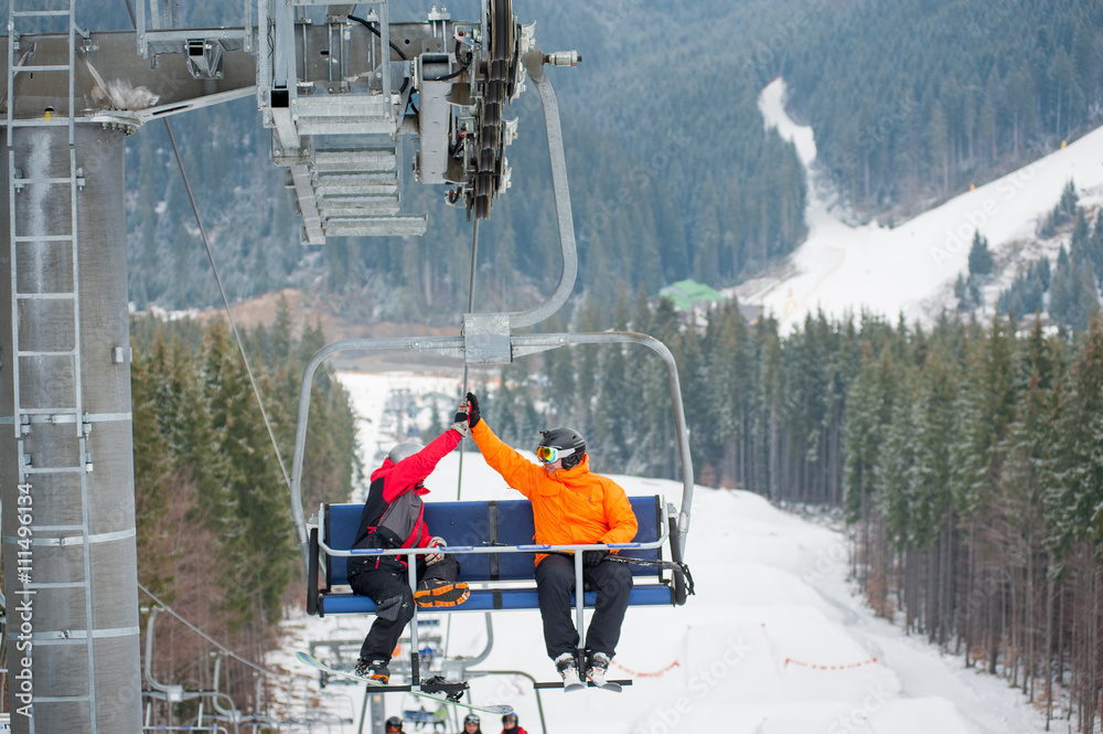 Fotka „Two male ride the ski chair lift up the mountain together and