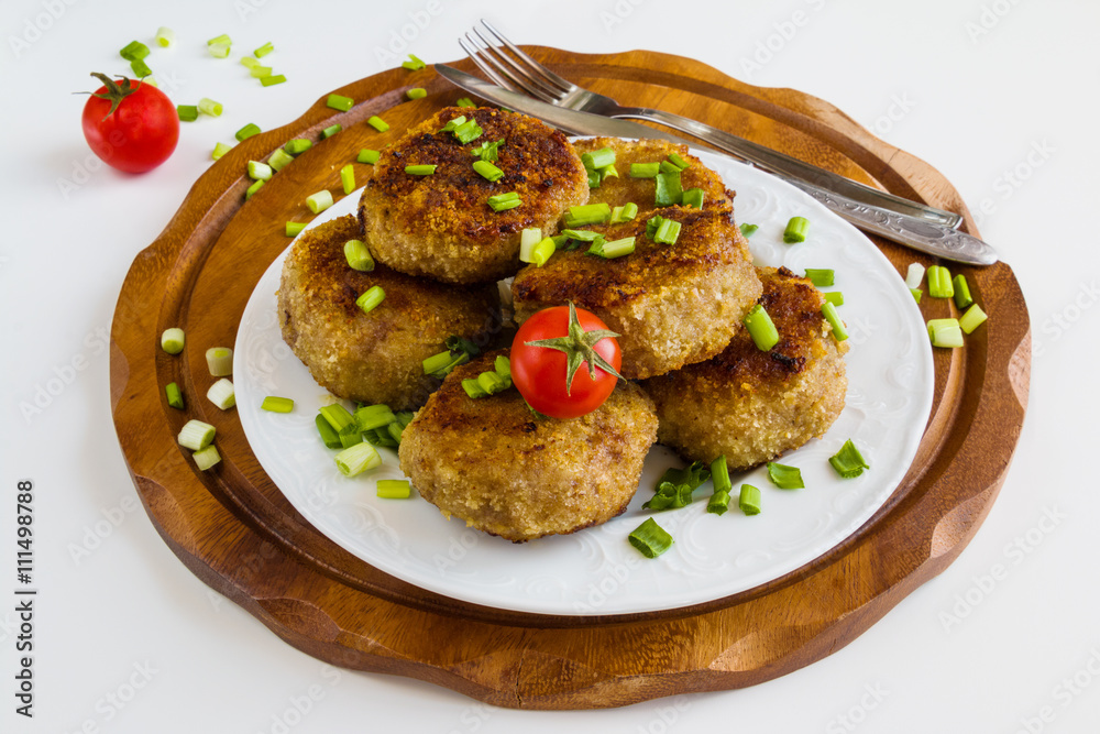 Roasted chicken cutlets with green onion on white plate and small cherry tomatoes on wooden background.