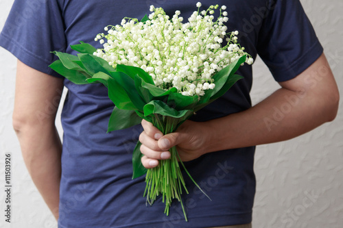 A man holding a bouquet of lilies of the valley for women. A man