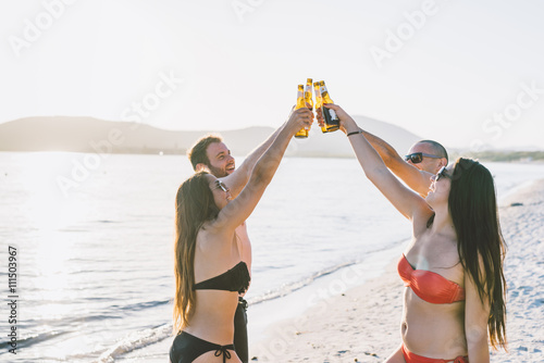 group of young multiethnic friends women and men at the beach in summertime toasting with some beers on the foreshore - friendship, relaxing, happy hour concepts