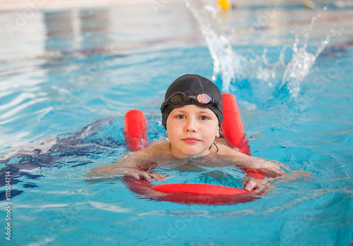 boy learn to swim with  red foam noodle in indoor pool
