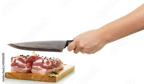 Raw pork with spices on cutting board, hand holding knife.