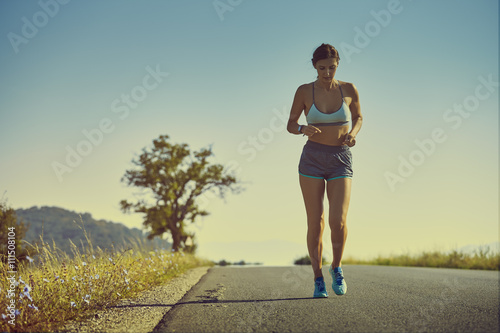 Beautiful fit woman in sport shorts running on a road at sunrise or sunset. Healthy lifestyle concept.