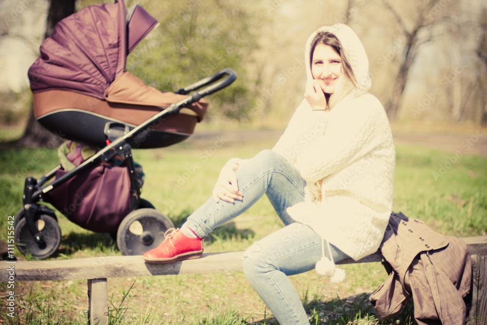 Smiling happy woman sitting on a bench with a pram in the background