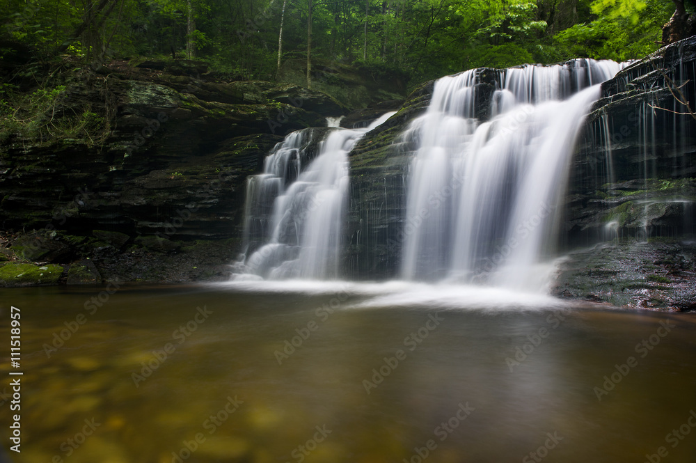 A long exposure of a waterfall scene in a forest of green trees.