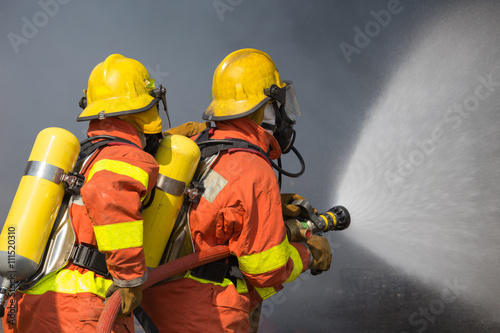 2 firefighters spraying water in fire fighting with dark smoke b