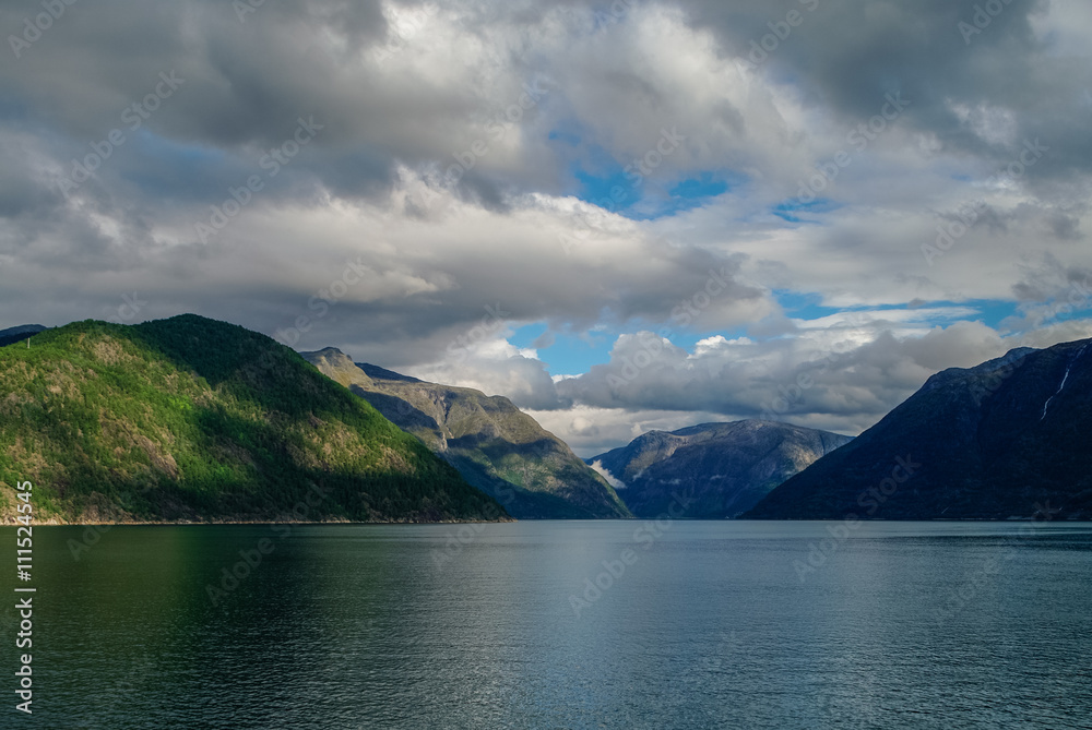 Cloudy sky over banks of fjord. Mountains with green forest, Eidfjord, Norway