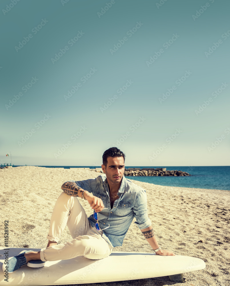 Handsome man sitting on surfboard at beach