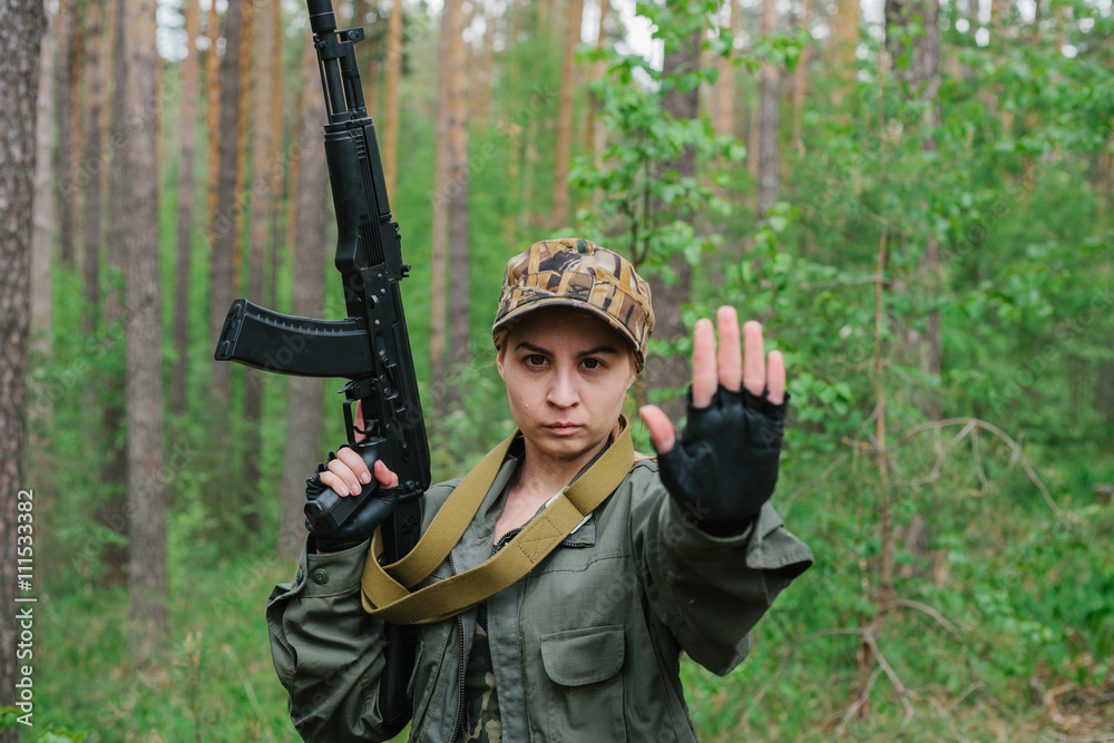 A woman soldier with a weapon shows a hand stop.