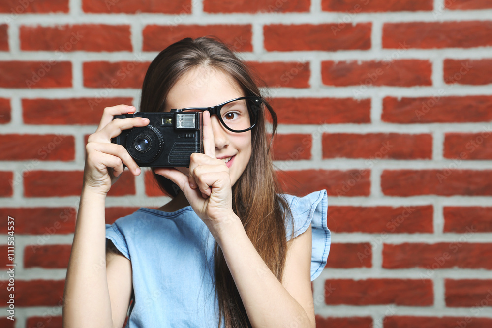Portrait of young girl with camera on brick wall background