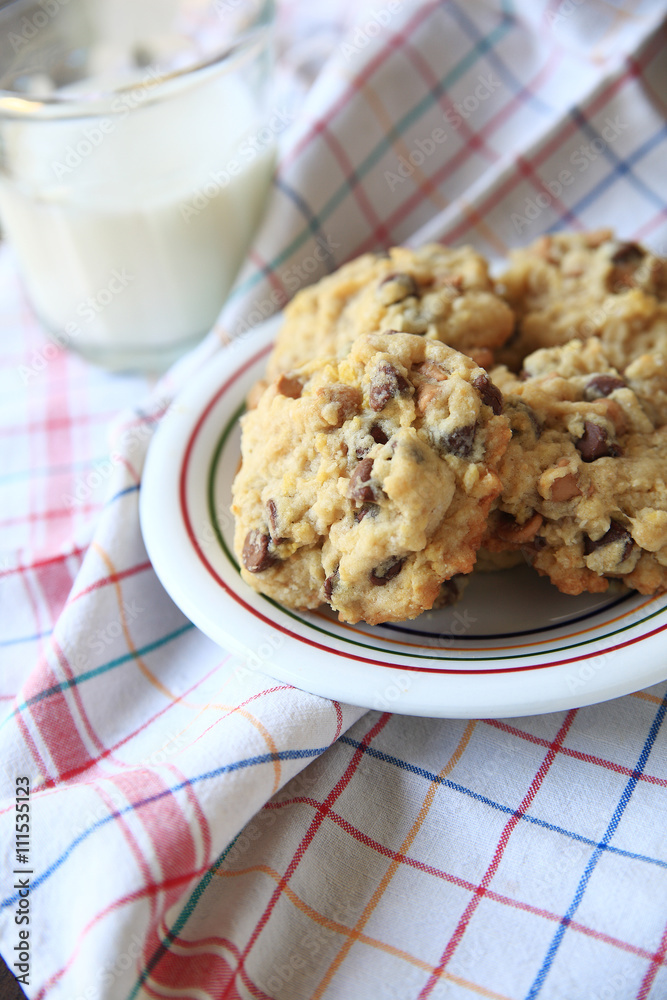 Chocolate and butterscotch chip cookies on a colorful dish with glass of milk on multi-colored dish cloth

