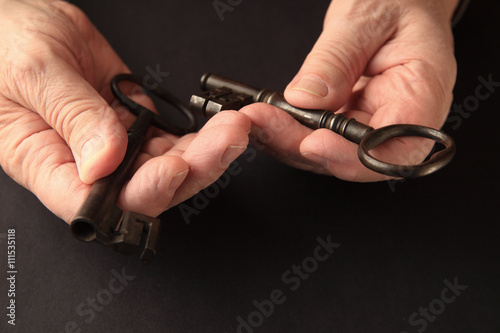 Older man holds two large, old keys on a black surface with copy space. 
