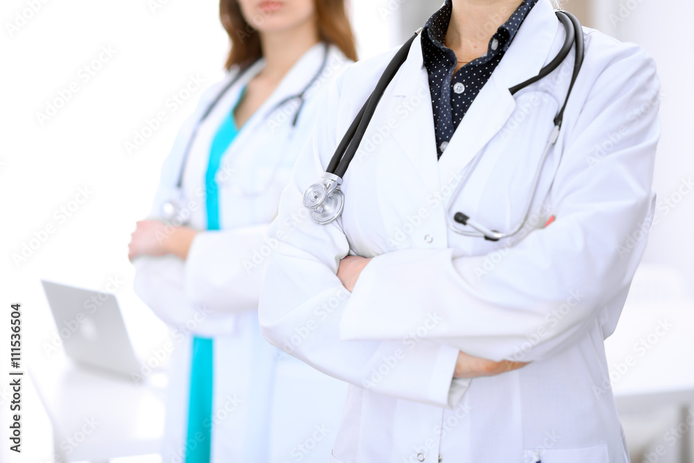 Close up of unknown female doctor standing in a hospital with her colleague in the background Close up of unknown female doctor standing in a hospital with her colleague in the background