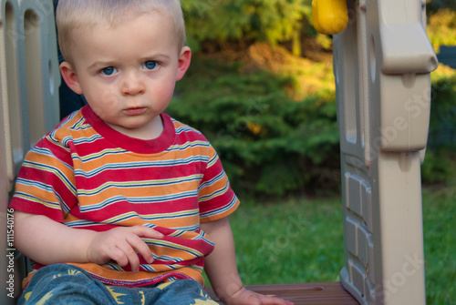 Serious Little Boy on Sitting on play structure in striped shirt