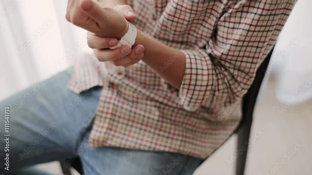 Man in plaid shirt with white watch, sitting on chair nervously make helpless gesture, touch watch, shake legs