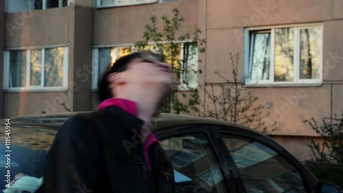 Brunette man in sunglasses wave head in camera on street in evening. Black jacket. Pink collar. Cheering photo