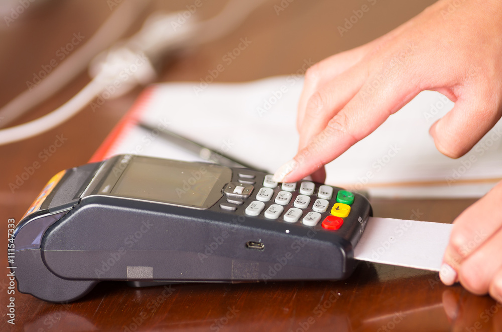 A woman hand operating a credit card machine, with card entering under the machine and a finger pressing a bottom A woman hand operating a credit card machine, with card entering under the machine and a finger pressing a bottom