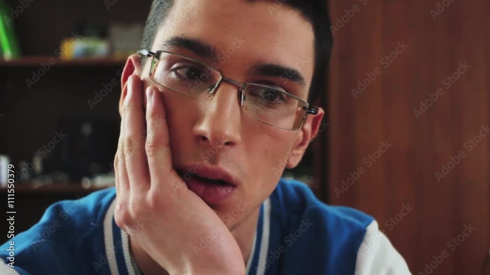 Portrait of young boy in glasses serious look in screen. Hold hand at cheek. Student. Boring. Tired. Teenager Portrait of young boy in glasses serious look in screen. Hold hand at cheek. Student. Boring. Tired. Teenager