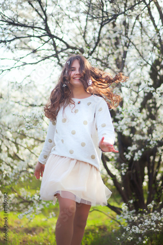 Young cheerful girl with long hair in tutu dancing in blossom garden