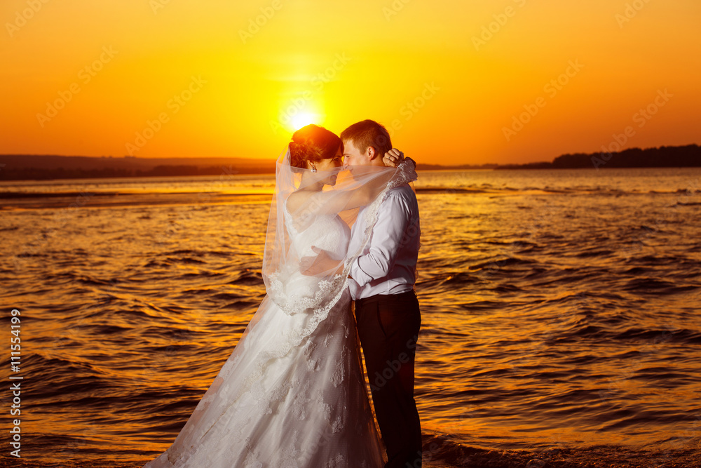 Beautiful wedding couple is kissing at golden tropical sunrise 
