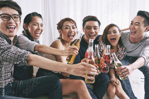 Cheerful Asian young people clinking bottles of beer photo