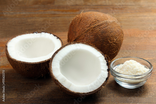 cut coconut with coconut flakes in glass bowl on brown wooden background