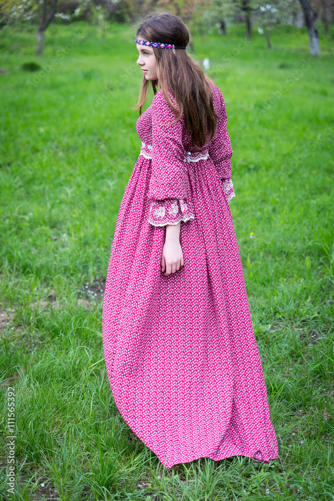Model passes through the city on foot. Young girl with long hair in beautiful long red dress with lace Model passes through the city on foot. Young girl with long hair in beautiful long red dress with lace