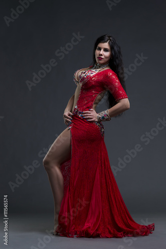 Young beautiful exotic eastern women performs belly dance in ethnic red dress on gray background