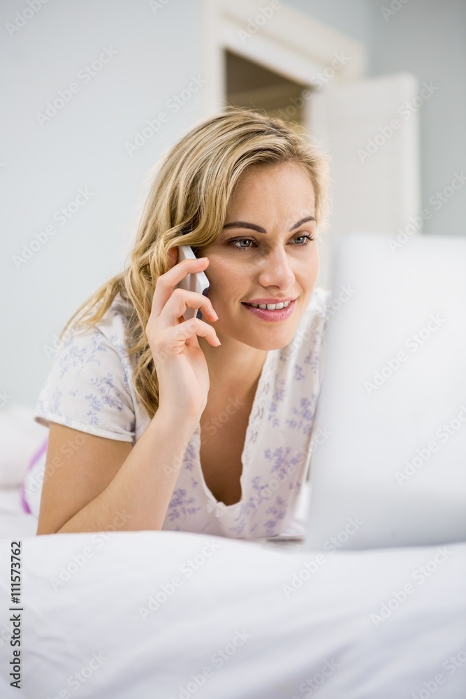 Woman using laptop while talking on mobile phone in bed Woman using laptop while talking on mobile phone in bed