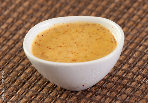 Close up of mustard sauce in white bowl over wooden surface.