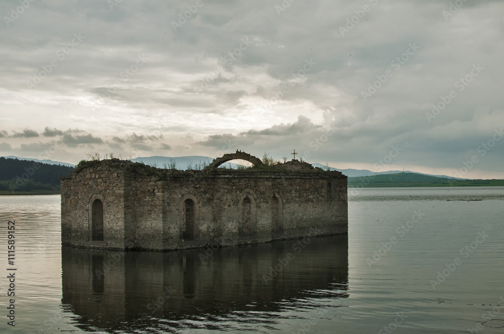 Abandoned destroyed stone orthodox church in dam waters amid cloudy sky background