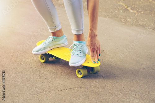 Girl rides on the road on a plastic skateboard in the sunlight