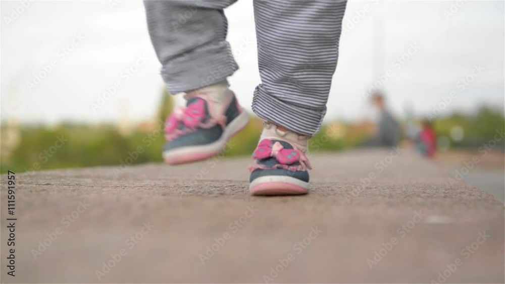 Little girl learning to walk with his mother, first steps, park, sunny day Little girl learning to walk with his mother, first steps, park, sunny day