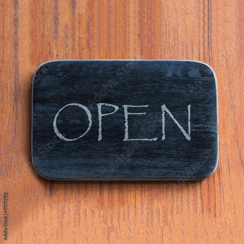 Black wooden board with "open" word against brown wood background.