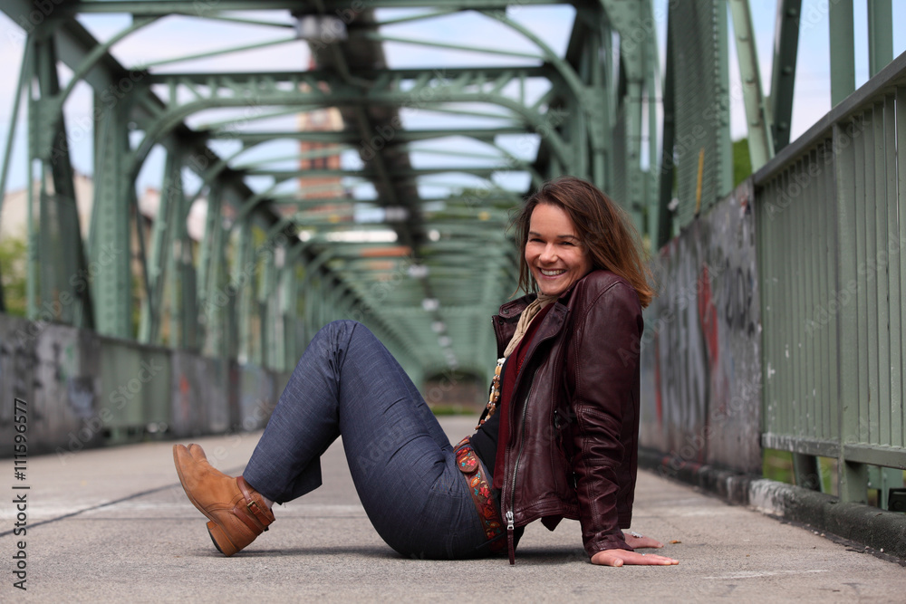 Beautiful brunette woman with leather jacket sitting on a bridge with graffiti Beautiful brunette woman with leather jacket sitting on a bridge with graffiti