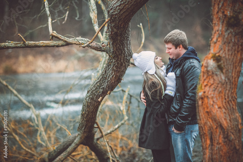 Beautiful young couple posing near lake and forest autumn. Woman in white gloves and cap.