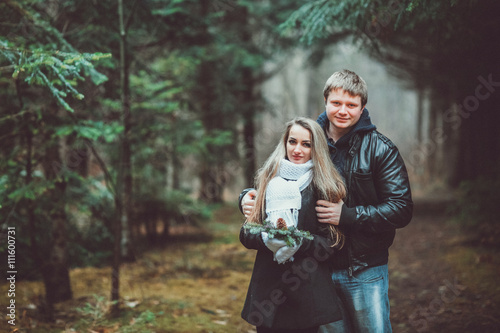 happy young loving couple in black leather jackets on the walk in pine forest. Woman in white gloves
