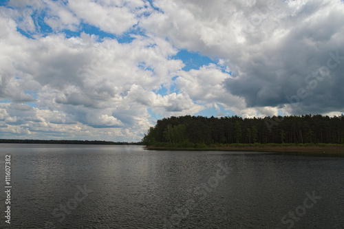 Scenic lake and forest.White clouds of different shapes are closing blue sky and sun  Pisochne ozero  Ukraine 