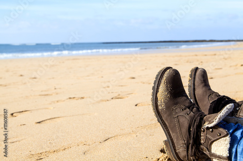 Füße in braunen Stiefeln an einem Strand an der an der Küste des leuchtend blauen Atlantik