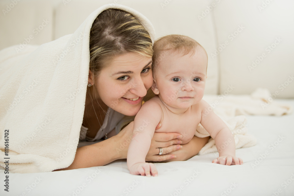 Portrait of happy young mother lying with her baby son under bla