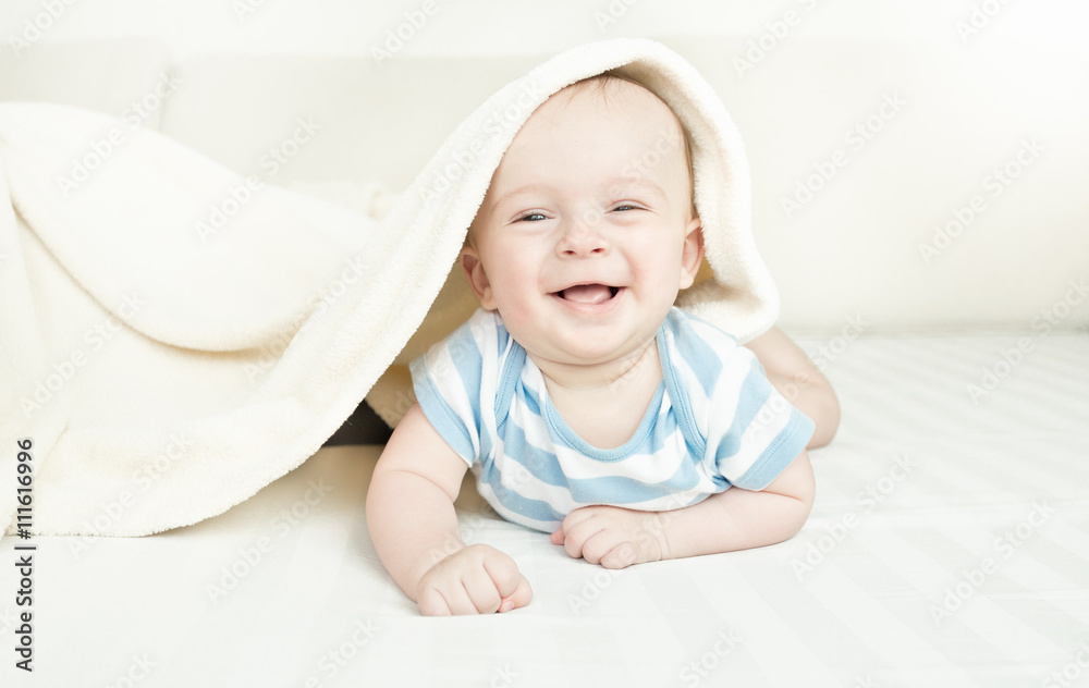 Cute laughing 6 month baby boy lying under the blanket Cute laughing 6 month baby boy lying under the blanket