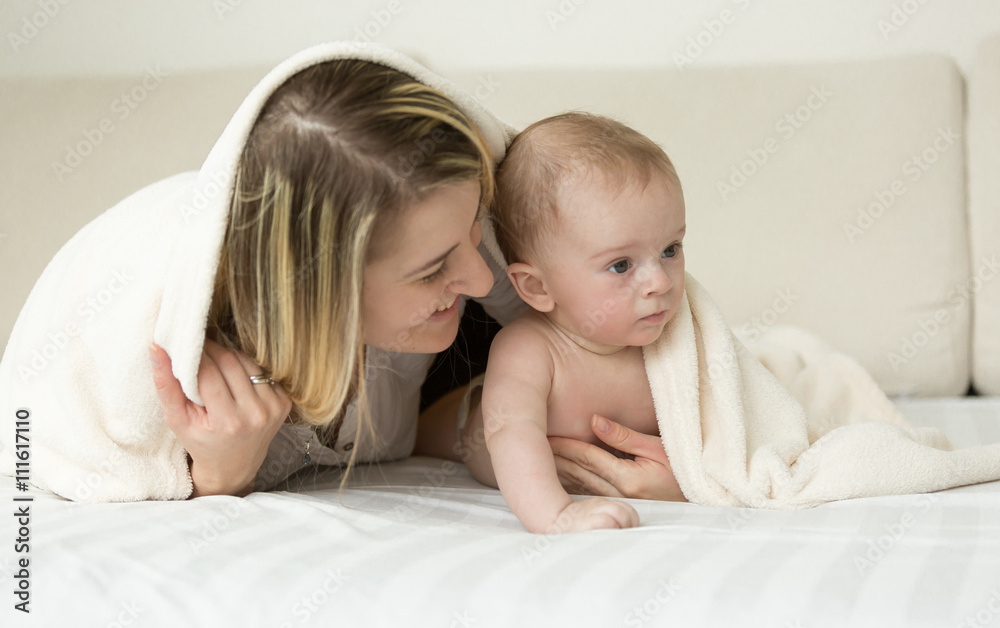 Portrait of smiling mother lying on bed with her baby son under Portrait of smiling mother lying on bed with her baby son under