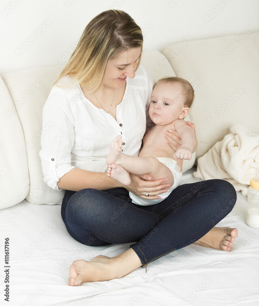 Beautiful mother sitting on bed with her cute baby boy Beautiful mother sitting on bed with her cute baby boy