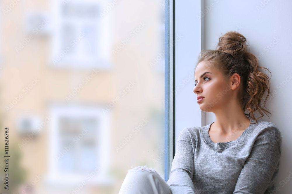 Fototapeta premium Beautiful young woman sitting on windowsill