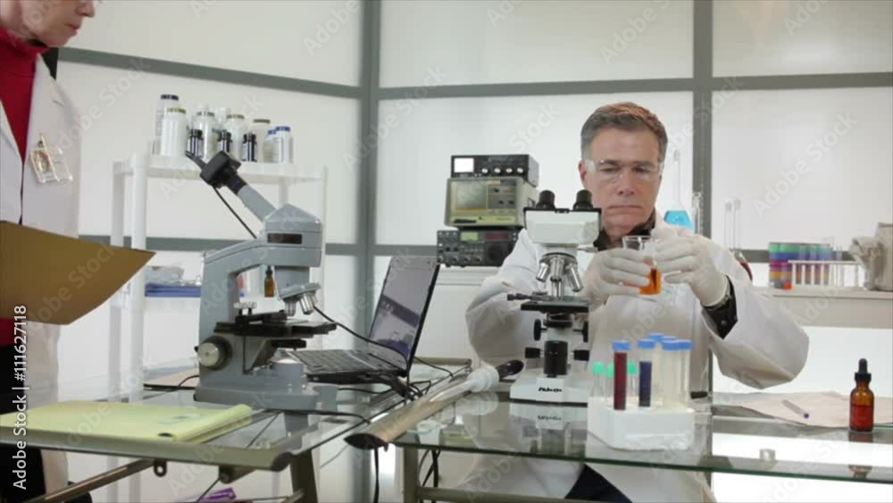 A woman scientist or chemist joins her colleague in a laboratory doing research with microscopes and other technologies. A woman scientist or chemist joins her colleague in a laboratory doing research with microscopes and other technologies.