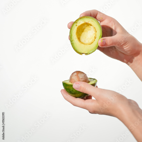 Hands holding fresh avocado cut in half on light background. Closeup 